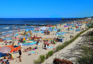 Drukke strand bij Ustronie Morskie met veelkleurige windschermen en gezinnen die genieten van de zee.