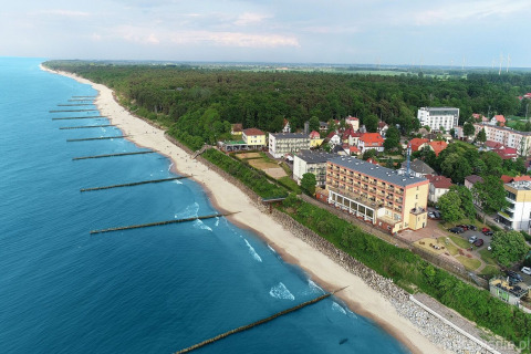 Luchtbeeld van het strand en de kustplaats Ustronie Morskie met hotels, bomen en de blauwe zee langs het bos.