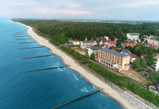 Luchtfoto van het strand en kustplaats Ustronie Morskie met hotels, bomen en de blauwe zee bij het bos.