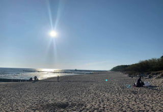 Zonnig strand in Ustronie Morskie vanaf een bungalow, met enkele mensen en kalme zee op de achtergrond.