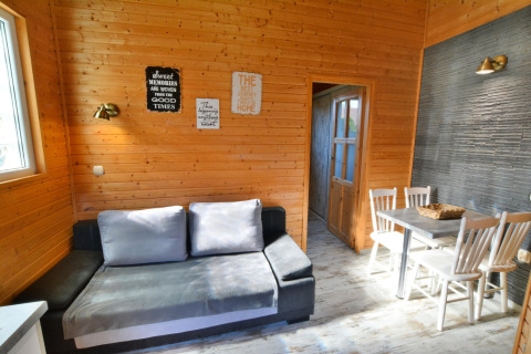 Woonkamer met houtmuren, grijze zetel, eettafel en vier stoelen in Older year-round cottage TYPE A Ustronie Morskie, Denemarken.