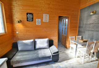 Woonkamer met houtmuren, grijze zetel, eettafel en vier stoelen in Older year-round cottage TYPE A Ustronie Morskie, Denemarken.