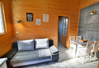 Wohnzimmer mit Holzwänden, grauem Sofa, Esstisch und vier Stühlen im Older year-round cottage TYPE A Ustronie Morskie, Dänemark.