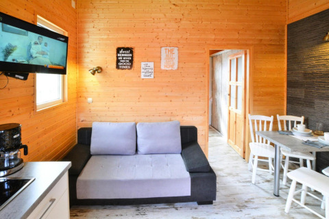 Lichte woonkamer in Older Cottage TYPE A Ustronie Morskie met houten wanden, bank, tv en eethoek.