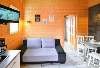 Lichte woonkamer in Older Cottage TYPE A Ustronie Morskie met houten wanden, bank, tv en eethoek.