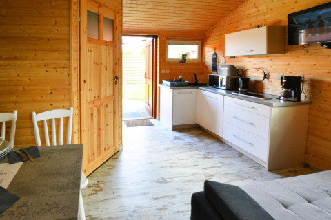 Cozy wooden cabin interior in Denmark featuring a modern kitchen, dining table, and open door with sunlight.