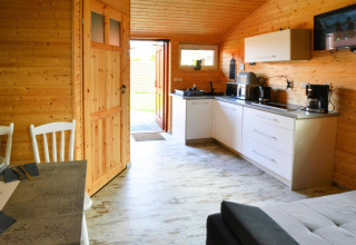 Sfeervol interieur van een houten huisje met moderne keuken, eettafel en open deur met zonlicht in Denemarken.