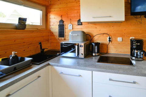Modern wooden cabin kitchen with sink, dish rack, microwave, kettle, and coffee maker on the countertop.
