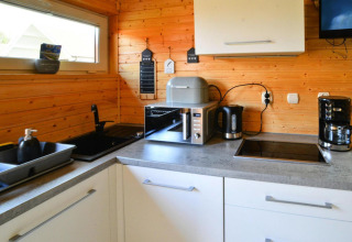 Moderne houten chaletkeuken met gootsteen, afdruiprek, microgolfoven, waterkoker en koffiezetapparaat.