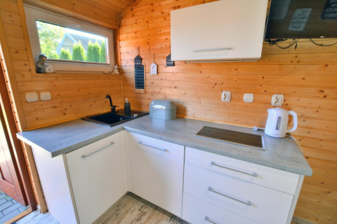 Gezellige keuken in een houten chalet met witte kasten, zwarte spoelbak, kookplaat en waterkoker.