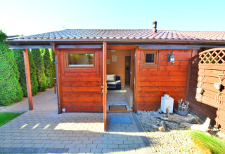 Wooden cabin with open door, paved patio, and greenery at Older year-round cottage TYPE A Ustronie Morskie.