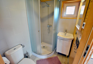 Modern cabin bathroom with shower enclosure, toilet, sink, small window, and wooden accented walls.