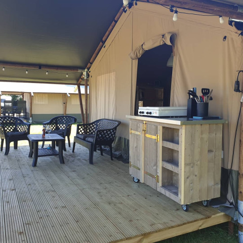 Veranda esterna con area salotto e mobile cucina davanti a una tenda safari di lusso attrezzata.