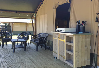 Udendørs terrasse med siddepladser og tekøkken foran en luksuriøs safariteltsindkvartering.
