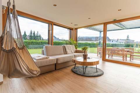 Modern lodge living room with hammock chair, sofa, large windows overlooking a green garden in Slovenia.