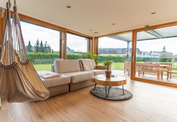 Hedendaagse lodge-living met hangstoel, sofa en grote ramen uitkijkend op tuin in Slovenië.