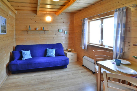 Accogliente casa vacanze in legno con divano blu, tavolo da pranzo e finestre, presso Holiday cottages Sarbinowo.