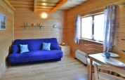Gemütliche Holzhütte mit blauer Couch, Esstisch, großen Fenstern und heller Einrichtung in Dänemark.