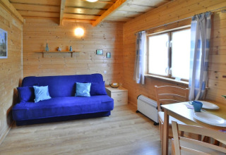 Houten chaletinterieur met blauwe zetel, eettafel en raam in Holiday cottages Sarbinowo in Denemarken.