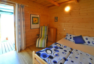 Camera da letto accogliente in legno con letto matrimoniale, biancheria colorata e poltrona vicino alla porta.