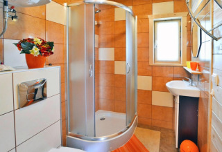 Bagno moderno presso Holiday cottages Sarbinowo in Danimarca, con box doccia, piastrelle arancioni e finestra.
