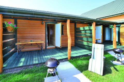 Buitenterras bij vakantiehuisjes in Sarbinowo, Denemarken, met barbecue, bank en grasveld.