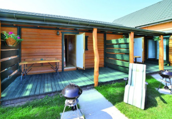Udendørs terrasse ved ferieboliger med grill, bænk og grøn græsplæne i Sarbinowo, Danmark.