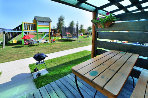 Overdekt terras met uitzicht op speeltuin, barbecue en grasveld bij Holiday cottages Sarbinowo op zonnige dag.