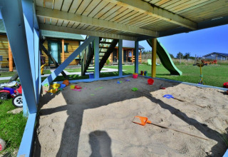 Parco giochi con sabbiera sotto un terrazzo in legno presso case vacanza Sarbinowo, Danimarca, giornata soleggiata.