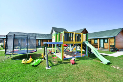 Parque infantil con columpios, tobogán y trampolín frente a cabañas en Holiday cottages Sarbinowo, Dinamarca.