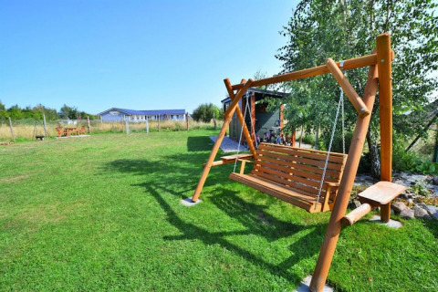 Vista all'aperto di una panchina a dondolo in legno su prato verde presso Holiday cottages Sarbinowo in Danimarca.