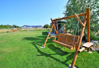 Vista all'aperto di una panchina a dondolo in legno su prato verde presso Holiday cottages Sarbinowo in Danimarca.