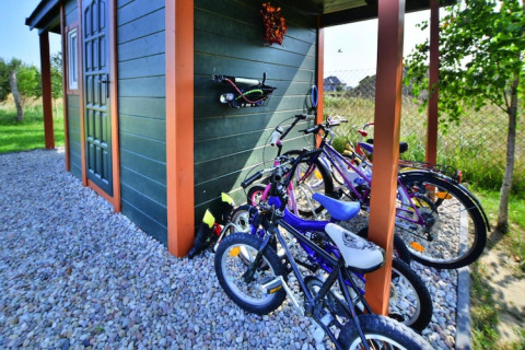 Fietsen geparkeerd naast een houten huisje bij Holiday cottages Sarbinowo, omgeven door grind en tuin.
