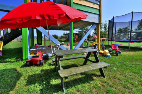 Area giochi nei Holiday cottages Sarbinowo, Danimarca, con giocattoli, tavolo da picnic e ombrellone rosso.