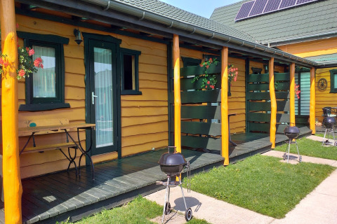 Holiday cottages in Sarbinowo with yellow walls, green doors, private porches, BBQ grills and flowers.