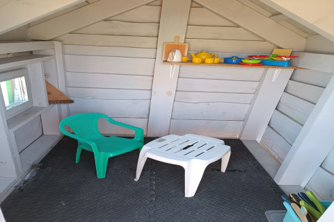 Interieur van een klein vakantiehuisje met een plastic stoel, tafel en speelgoedkeukenspullen op de plank.