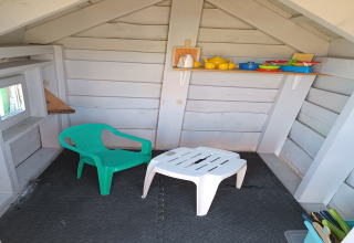 Binnenkant van een klein vakantiehuisje met een plastic stoel, tafel en speelgoedservies op de plank.