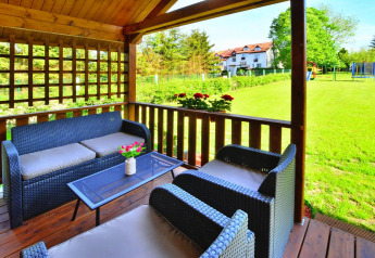 Terraza cubierta de madera con muebles de mimbre y vistas al jardín en cabañas de verano en Ustronie Morskie.
