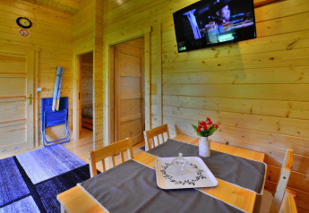 Vista interior de una cabaña de verano con paredes de madera, mesa de comedor, TV y flores.