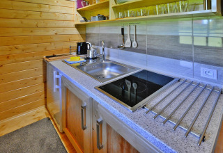 Modern kitchenette in a wooden cabin with induction cooktop, sink, utensils, and open shelving.