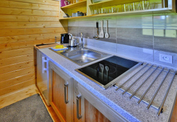 Cocina moderna en cabaña de madera con vitrocerámica, fregadero, utensilios y estantes abiertos.
