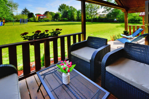 Cozy patio with wicker chairs, flowers on the table, overlooking a large lawn at a summer cottage lodge.