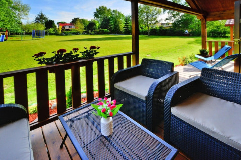Sunny wooden terrace with outdoor seating overlooking a spacious green lawn at summer cottages in Ustronie Morskie.