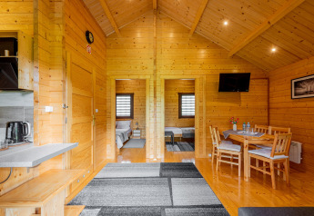Vista interior de una cabaña de madera en Ustronie Morskie, con comedor, cocina y dormitorios visibles.