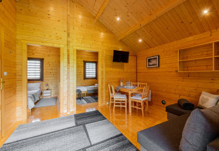 Interior of a summer cottage for 5 people with wooden walls, dining area, sofa, TV, and two bedrooms.