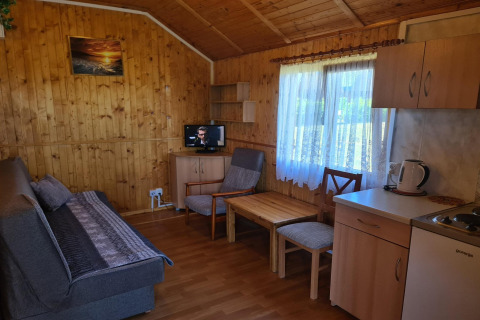 Cozy Jarosławiec single-storey cabin interior with wood paneling, sofa, dining area, kitchenette, and TV.