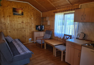 Knusse Jarosławiec bungalow met houten wanden, bank, eettafel, keukenblok en raam met lichte gordijnen.