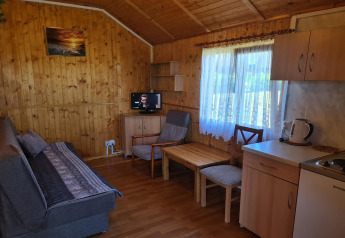 Salon chaleureux dans un chalet Jarosławiec de plain-pied, murs boisés, canapé, coin cuisine et fenêtre.