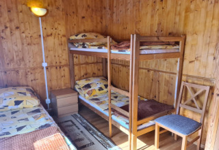 Habitación de cabaña revestida de madera con litera, cama individual, silla y mesa de noche en Dinamarca.
