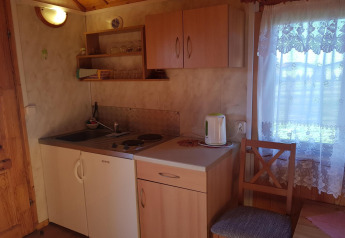 Petite kitchenette de chalet avec meubles en bois, bouilloire électrique et fenêtre ornée de rideaux en dentelle.